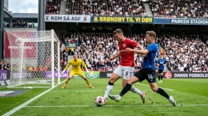 Fodboldkamp i gang pa stadion med spillere fra to hold der kaemper om bolden foran malet